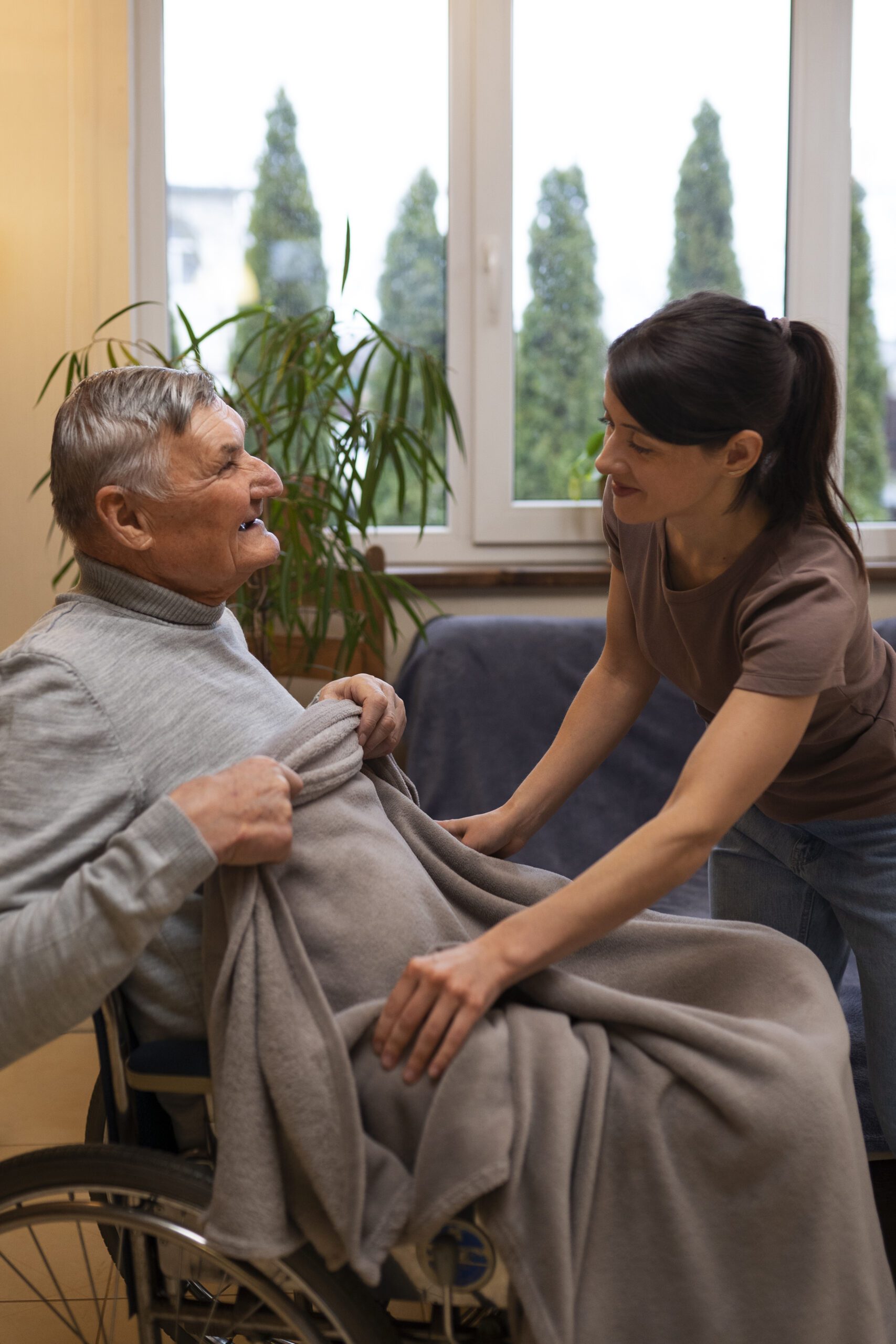 A compassionate caregiver assisting an elderly man in a wheelchair by covering him with a warm blanket, representing high-quality Companion Care in Philadelphia.