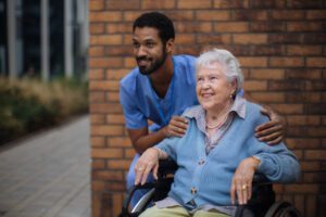 A compassionate caregiver assisting an elderly man in a wheelchair by covering him with a warm blanket, representing high-quality Companion Care in Philadelphia.